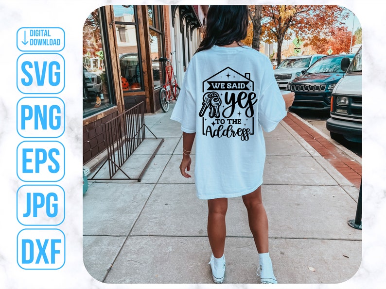 Op de afbeelding: Wit T-shirt met een zwart grafisch ontwerp van een huis met de tekst "We said yes to the address".