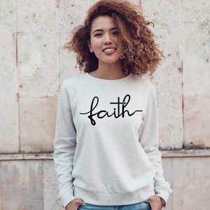 May include: A white sweatshirt with the word "faith" written in black cursive lettering. The word "faith" has a cross incorporated into the letter "t".