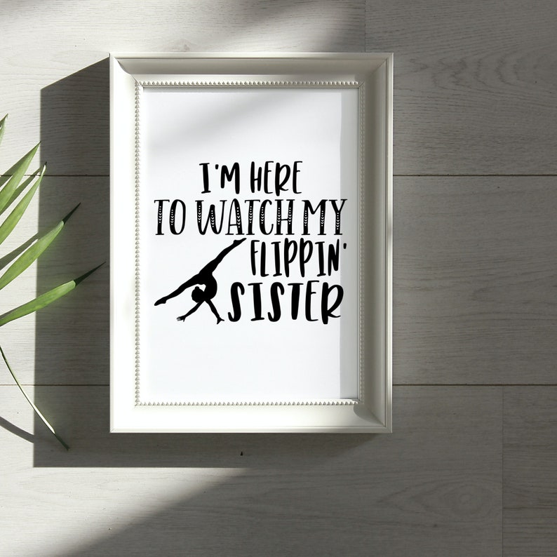 May include: White framed print with black text that reads "I'm here to watch my flippin' sister". A black silhouette of a gymnast performing a back handspring is in the center of the text.