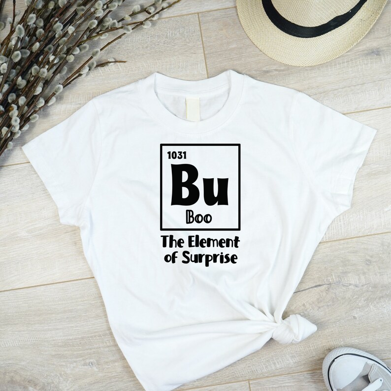 K&ouml;nnte beinhalten: Wei&szlig;es T-Shirt mit einer schwarzen Grafik eines Elements aus dem Periodensystem. Das Element ist mit "Bu" beschriftet, mit dem Namen "Boo" und dem Text "The Element of Surprise".