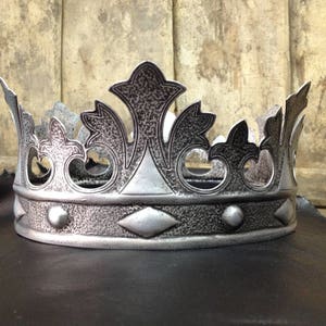 Peut inclure: Une couronne en argent avec une surface textur&eacute;e et des d&eacute;tails complexes. La couronne a un sommet pointu et une bande avec des accents d&eacute;coratifs.