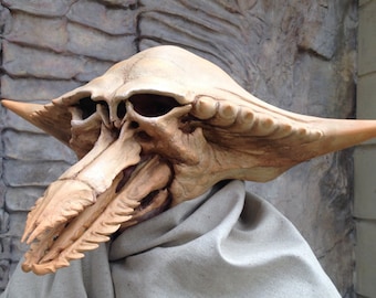 May include: A detailed, beige-colored, skeletal mask with a long, pointed beak and intricate details. The mask is made of a hard material and appears to be a prop or costume piece.