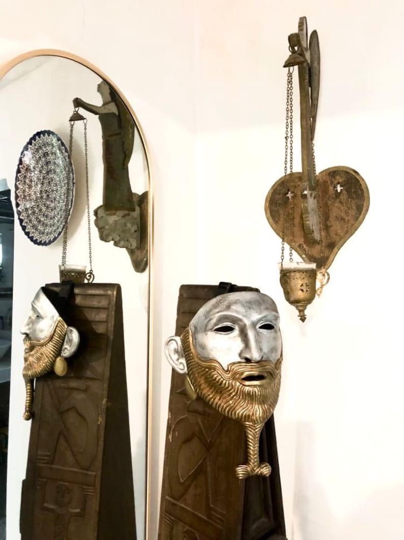 May include: Two silver and gold masks with beards on wooden panels. The masks have a realistic human face with a silver face and a gold beard. The masks are hanging on the wall.