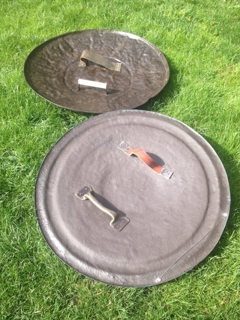 May include: Two round, brown shields with metal handles. The shields are made of a textured material and have a slightly raised edge.