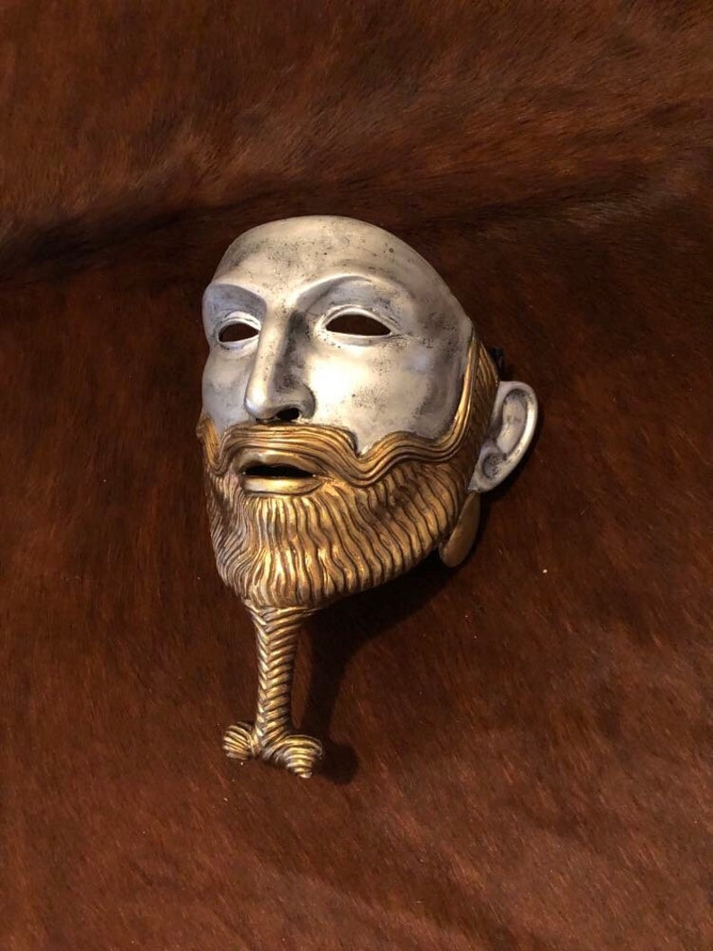 May include: A silver and gold mask with a beard. The mask has a human face with a long, braided beard.