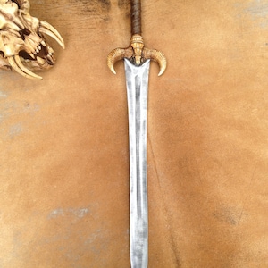 May include: A silver sword with a brown leather handle and a gold-colored pommel. The sword has a decorative design on the pommel that resembles horns.