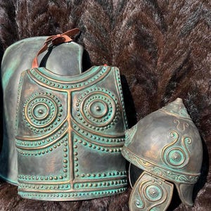 Peut inclure: Un plastron, un casque et une pièce dorsale de couleur bronze avec des motifs en relief complexes. L'armure présente une patine vert-de-gris, avec une sangle en cuir sur la pièce dorsale. Le casque présente un motif tourbillonnant décoratif.