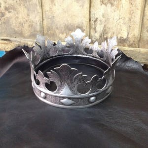 Peut inclure: Une couronne argent&eacute;e avec un design d&eacute;coratif. La couronne a un sommet pointu et une base circulaire.