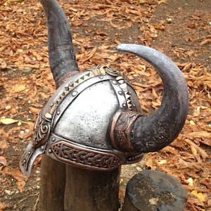 May include: A silver and copper Viking helmet with two large horns. The helmet has intricate details and is decorated with a braided copper band.