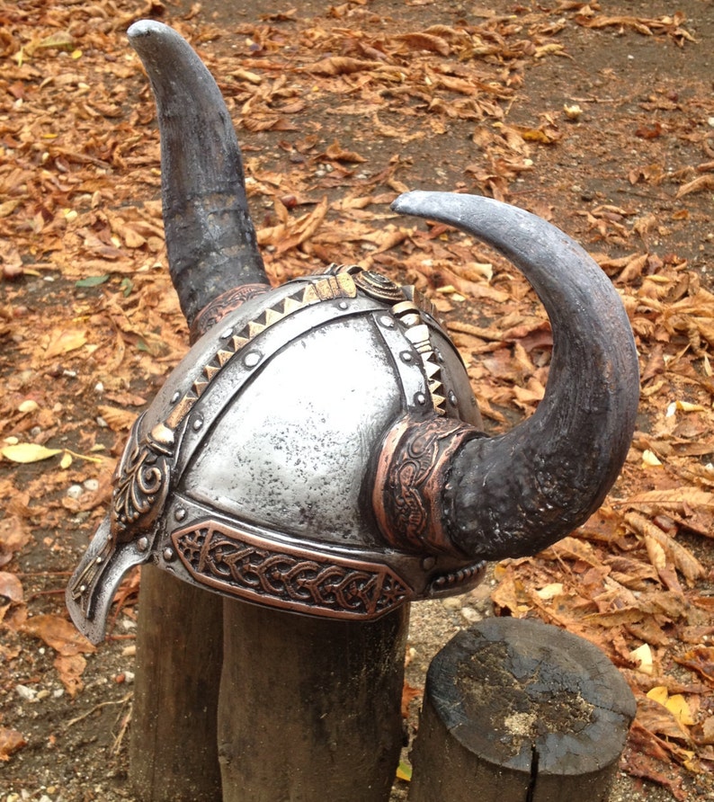 May include: A silver and copper Viking helmet with two large horns. The helmet has intricate details and is decorated with a braided copper band.