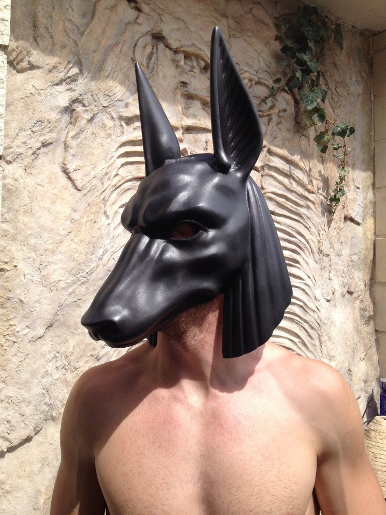 May include: A black Anubis mask with long, pointed ears. The mask is made of a smooth, hard material and has a realistic, detailed design.
