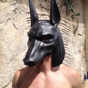 May include: A black, realistic-looking Anubis mask with a textured surface. The mask has large, pointed ears and a long snout.