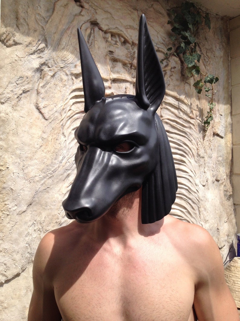 May include: A black, realistic-looking Anubis mask with a textured surface. The mask has large, pointed ears and a long snout.
