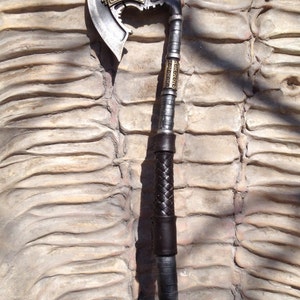 May include: A silver and gold axe with a black leather wrapped handle. The axe head has a decorative design and the handle has a braided leather wrap.