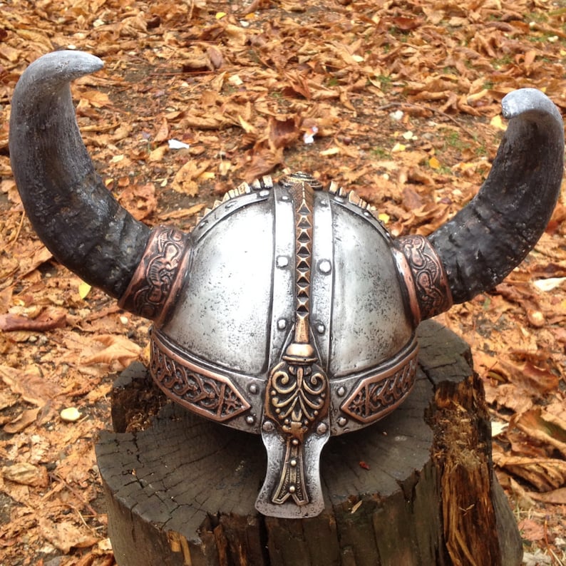May include: A silver and copper Viking helmet with horns. The helmet has intricate details and a decorative design.