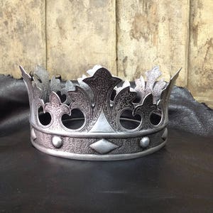 Peut inclure: Une couronne argent&eacute;e avec un motif d&eacute;taill&eacute; de feuilles et un motif en forme de diamant. La couronne a une surface textur&eacute;e et est en m&eacute;tal.