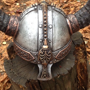 May include: A silver Viking helmet with a copper trim and horns. The helmet has a decorative design on the front and a pointed top.