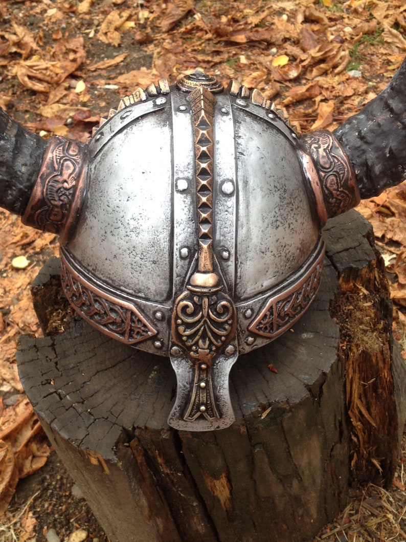 May include: A silver Viking helmet with a copper trim and horns. The helmet has a decorative design on the front and a pointed top.