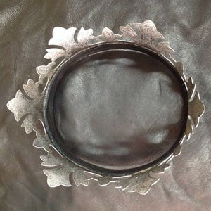 Peut inclure: Une couronne en m&eacute;tal argent&eacute; avec un design d&eacute;coratif et orn&eacute;. La couronne est circulaire et a une finition lisse et polie.
