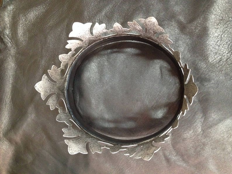 Peut inclure: Une couronne en m&eacute;tal argent&eacute; avec un design d&eacute;coratif et orn&eacute;. La couronne est circulaire et a une finition lisse et polie.