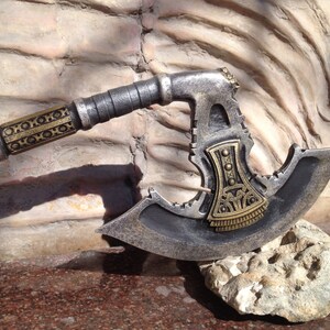 May include: A silver and gold axe with a decorative handle. The axe head has a unique design with a serrated edge and a gold accent.