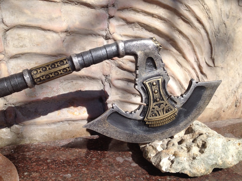 May include: A silver and gold axe with a decorative handle. The axe head has a unique design with a serrated edge and a gold accent.