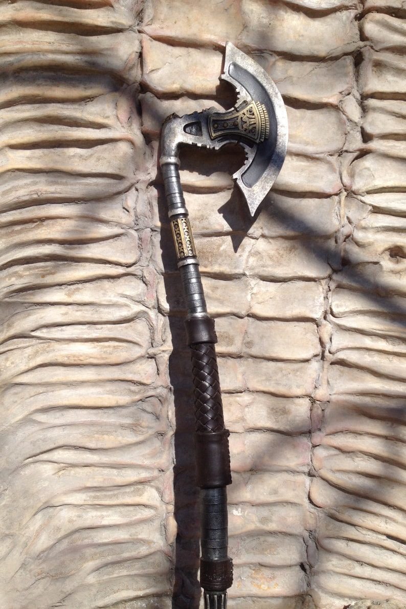 May include: A silver and black axe with a leather wrapped handle. The axe head has a decorative design with gold accents.
