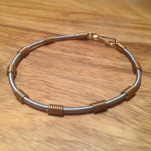 Könnte beinhalten: Ein silbernes Armband mit goldenen Akzenten. Das Armband besteht aus einem gewickelten Metalldraht und hat einen Verschluss.