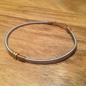 Peut inclure: Un bracelet argenté fait d'une corde de guitare avec des accents dorés.