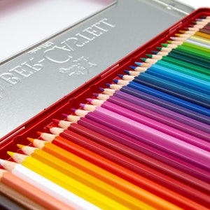 May include: A tin box of coloured pencils with the brand name "Derwent-Craylett" printed on the lid. The pencils are arranged in a rainbow pattern, with red, orange, yellow, green, blue, indigo, and violet.