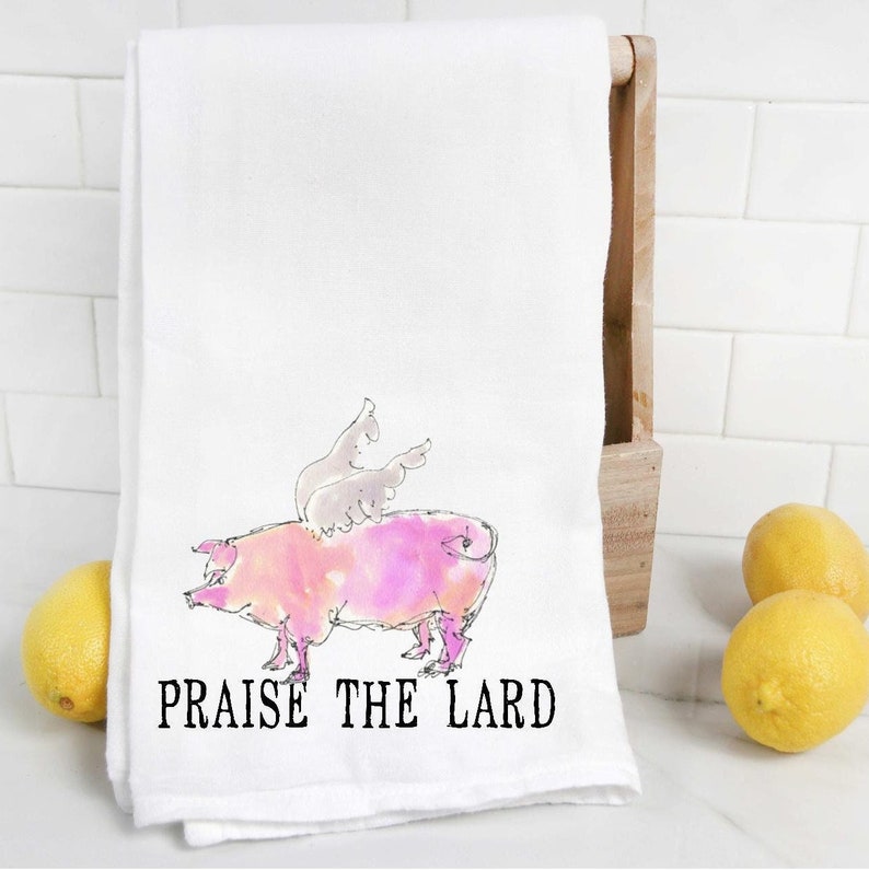 May include: White kitchen towel with a pink pig with wings and the text "Praise the Lard".
