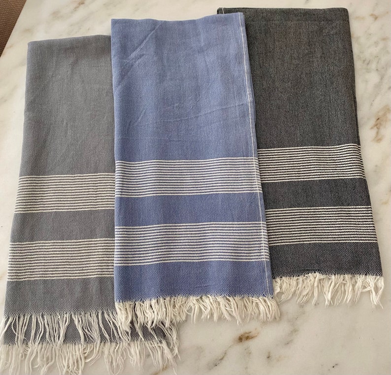 K&ouml;nnte beinhalten: Drei gestreifte Handt&uuml;cher in Grau, Blau und Schwarz mit wei&szlig;en Streifen. Die Handt&uuml;cher haben einen Fransenrand.