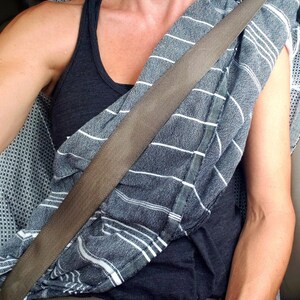 K&ouml;nnte beinhalten: Eine Person tr&auml;gt ein schwarzes Tanktop mit einem wei&szlig;-grauen gestreiften Schal, der um den Hals gebunden ist. Ein brauner Sicherheitsgurt verl&auml;uft diagonal &uuml;ber die Brust.
