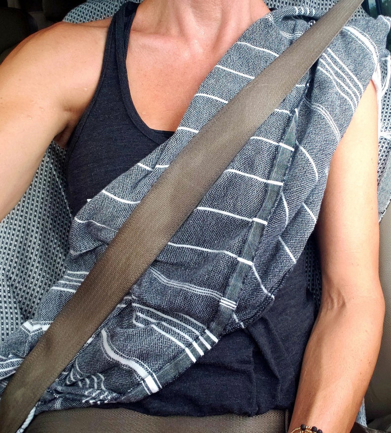 K&ouml;nnte beinhalten: Eine Person tr&auml;gt ein schwarzes Tanktop mit einem wei&szlig;-grauen gestreiften Schal, der um den Hals gebunden ist. Ein brauner Sicherheitsgurt verl&auml;uft diagonal &uuml;ber die Brust.