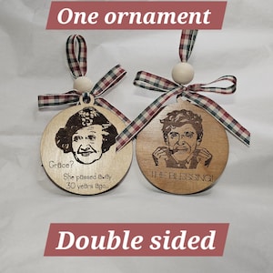 May include: Two wooden, double-sided ornaments with engraved portraits and text. One says "Grace? She passed away 30 years ago..." and the other says "THE BLESSING!". Each has a plaid ribbon and wooden bead.