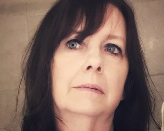 May include: A woman with dark brown hair and blue eyes is wearing a floral print blouse. She is looking up and to the right.