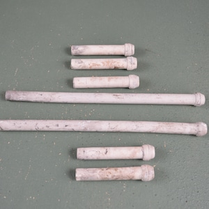 May include: A set of eight white wooden dowels with rounded ends. The dowels are of varying lengths and are arranged in a staggered pattern on a green surface.