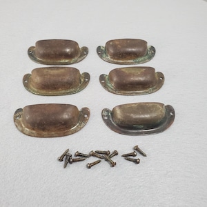 May include: Six semi-oval metal drawer pulls with a weathered, dark brown patina and visible green oxidation. Each pull features two side mounting holes and a rounded handle grip. A collection of small, matching metal screws is included below.