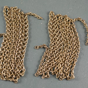 May include: Two sections of gold-colored chain are displayed against a gray background. Each chain section is composed of numerous interlocking links, creating a textured appearance. The chains are likely for jewelry or decorative purposes.