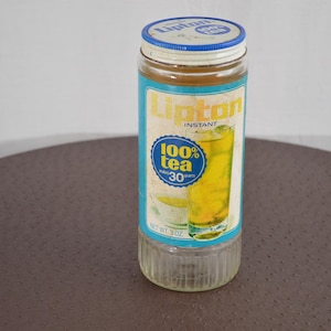 May include: A glass jar of Lipton Instant 100% Tea with 30 tea bags. The jar has a blue lid with the Lipton logo and a blue and yellow label with a glass of iced tea.
