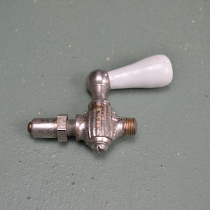 May include: A silver and white vintage faucet with a porcelain handle. The faucet has a threaded end and a round knob.