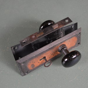 May include: A vintage door lock and handle set with black porcelain knobs and a brass key. The lock is made of metal and has a rusty patina.