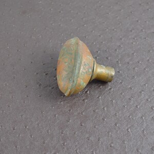 May include: An antique brass door knob with a weathered, aged appearance. The knob has a rounded, oval shape with a short, cylindrical stem. The brass has a mix of orange and green patina.
