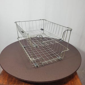 May include: Two-tier wire metal storage baskets. The baskets are rectangular with a grid pattern and are stacked on top of each other. The baskets are silver and sit on a brown surface.