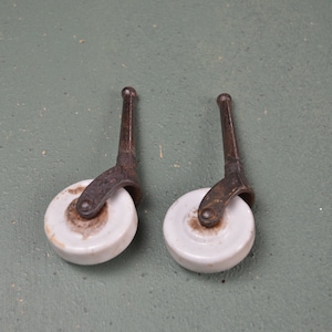 May include: Two antique white porcelain caster wheels with rusty metal stems. The wheels are about 2 inches in diameter.