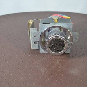 May include: A silver microphone with a black mesh grille and a chrome casing. The microphone is attached to a metal frame with wires.