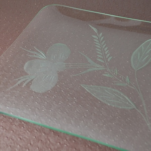 May include: A clear glass square serving tray with an etched floral design. The design features a flower with three petals and leaves.