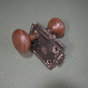 May include: A vintage black metal door lock with two wooden knobs. The lock has a decorative design and is in good condition.