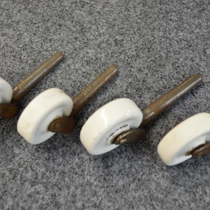May include: Five white porcelain caster wheels with metal stems. The wheels have a metal axle and a metal ring around the edge.