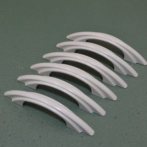 May include: Six white ceramic cabinet knobs with a curved, arched design. The knobs are arranged in a staggered pattern.